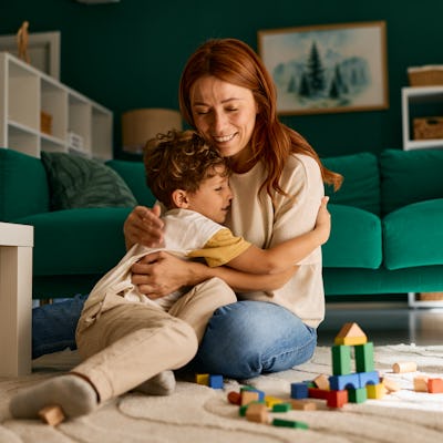 A mom hugs her son while playing block on the living room floor.