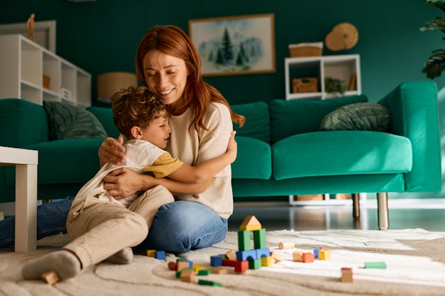A mom hugs her son while playing block on the living room floor.