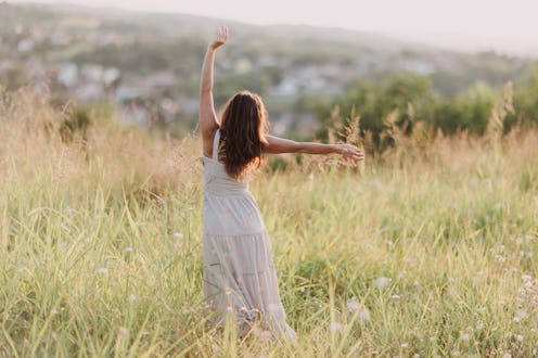 A young woman joyfully dances in a green meadow under soft sunlight, surrounded by nature.