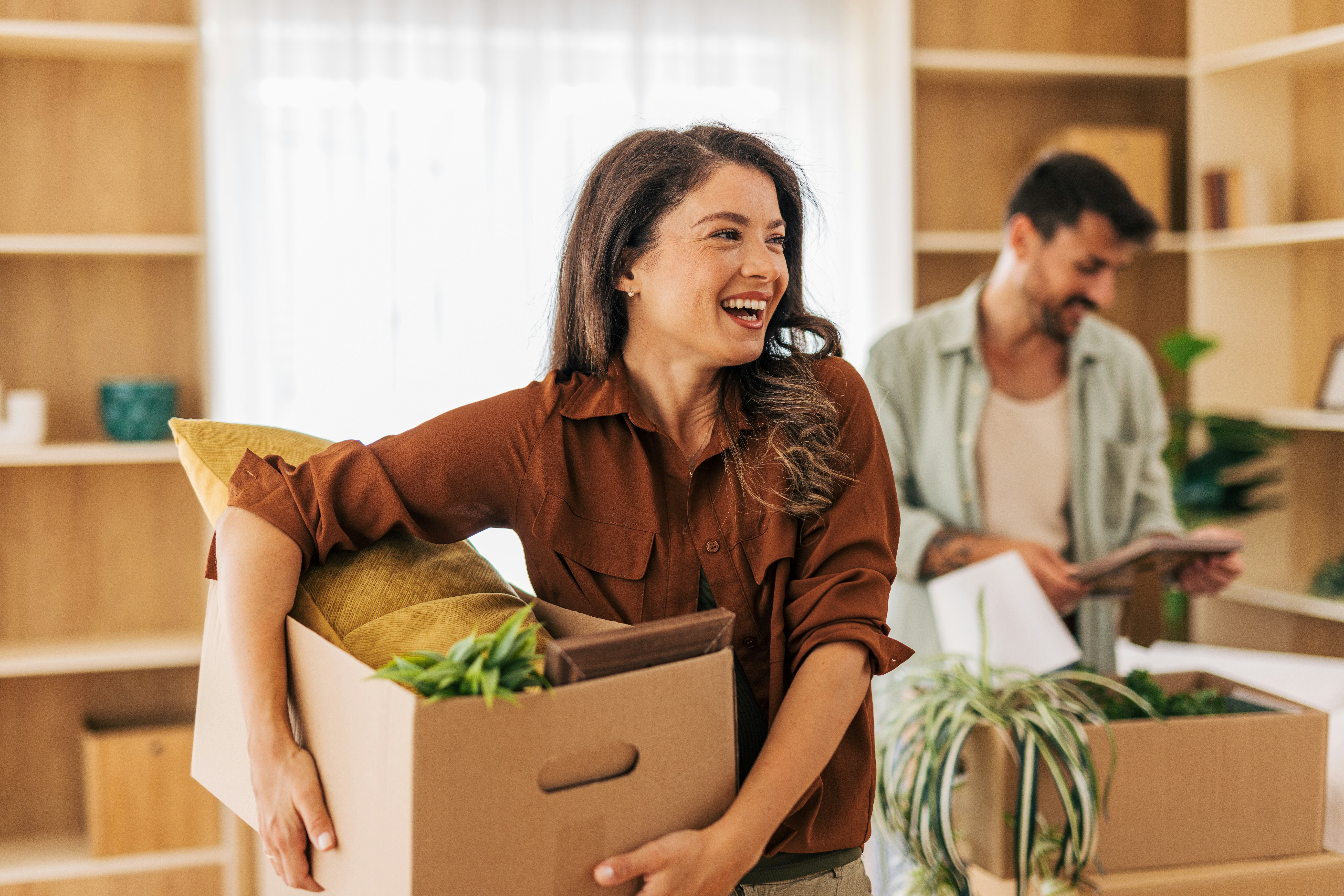 Young couple smiling and carrying boxes filled with belongings into a new apartment, embracing the e...