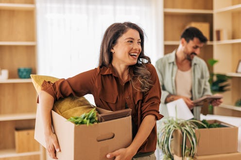 Young couple smiling and carrying boxes filled with belongings into a new apartment, embracing the e...