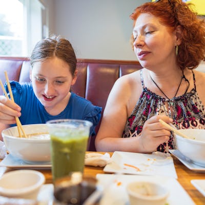 A mom and her daughter enjoy a lunch of noodle soup at a restaurant.