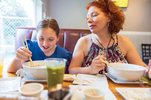 A mom and her daughter enjoy a lunch of noodle soup at a restaurant.