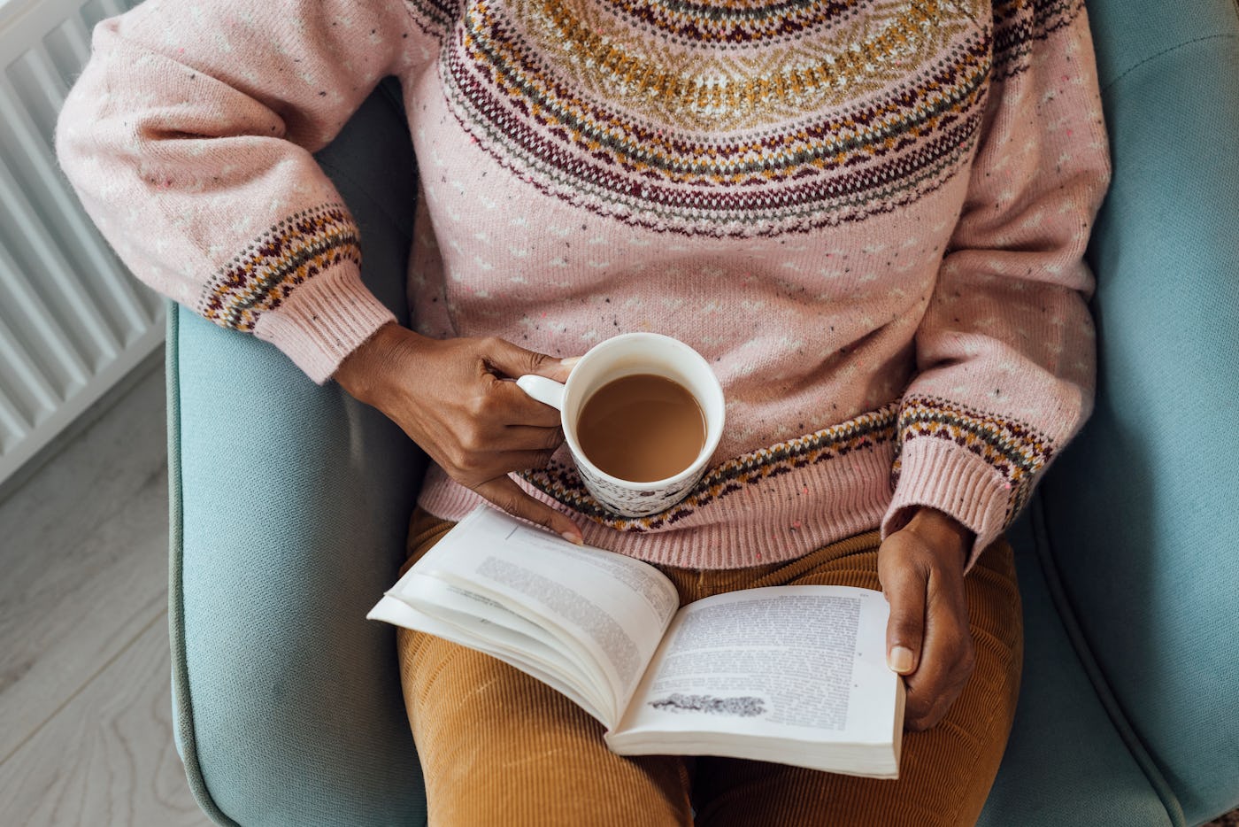 A high angle view of a mature woman sitting in a holiday rental. She is reading a book and has a hot drink she is enjoying as she sits. She is in a holiday home in the Scottish Highlands.