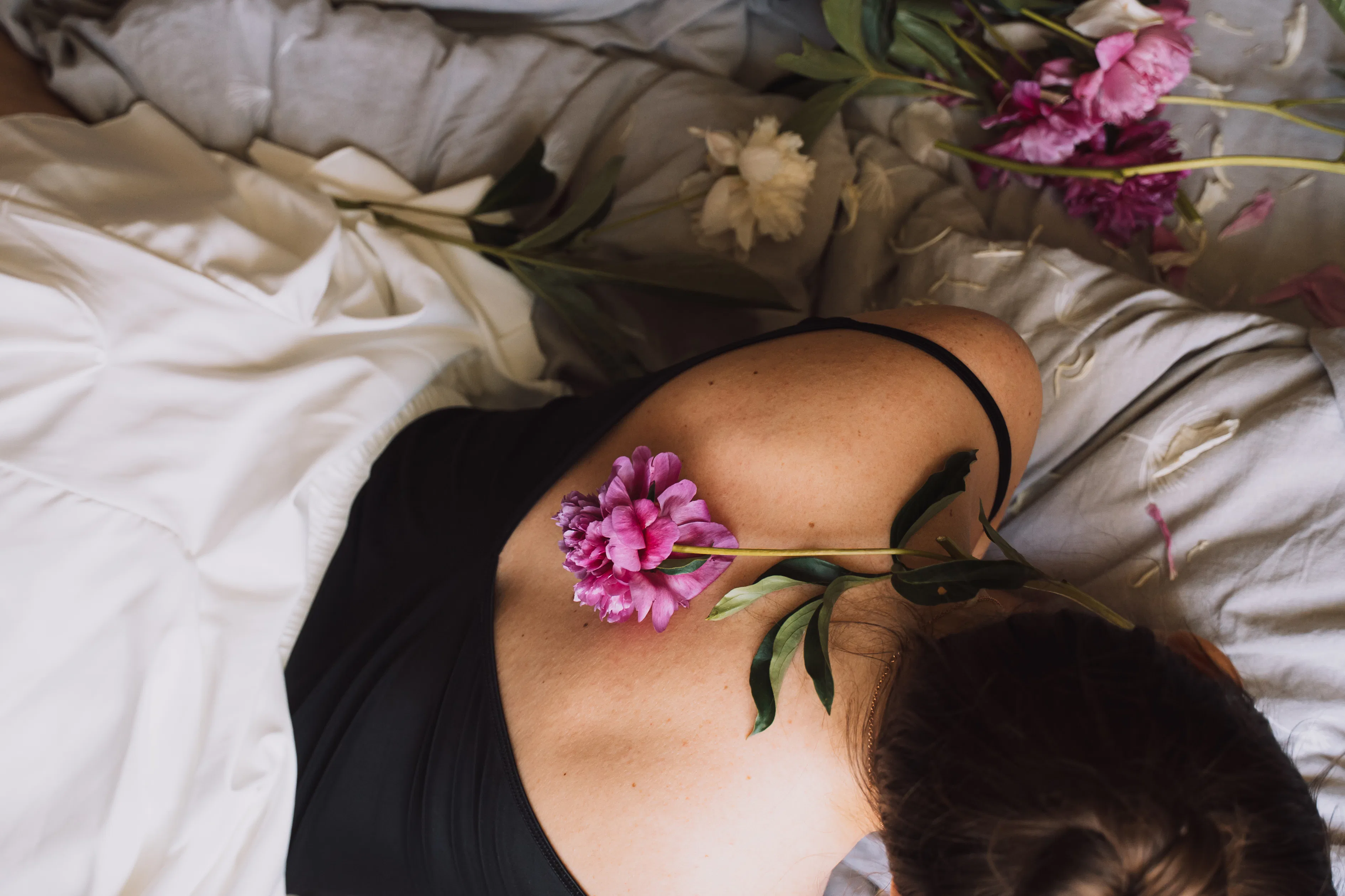 Close overhead view of a bright peony placed along the woman’s spine on soft sheets.