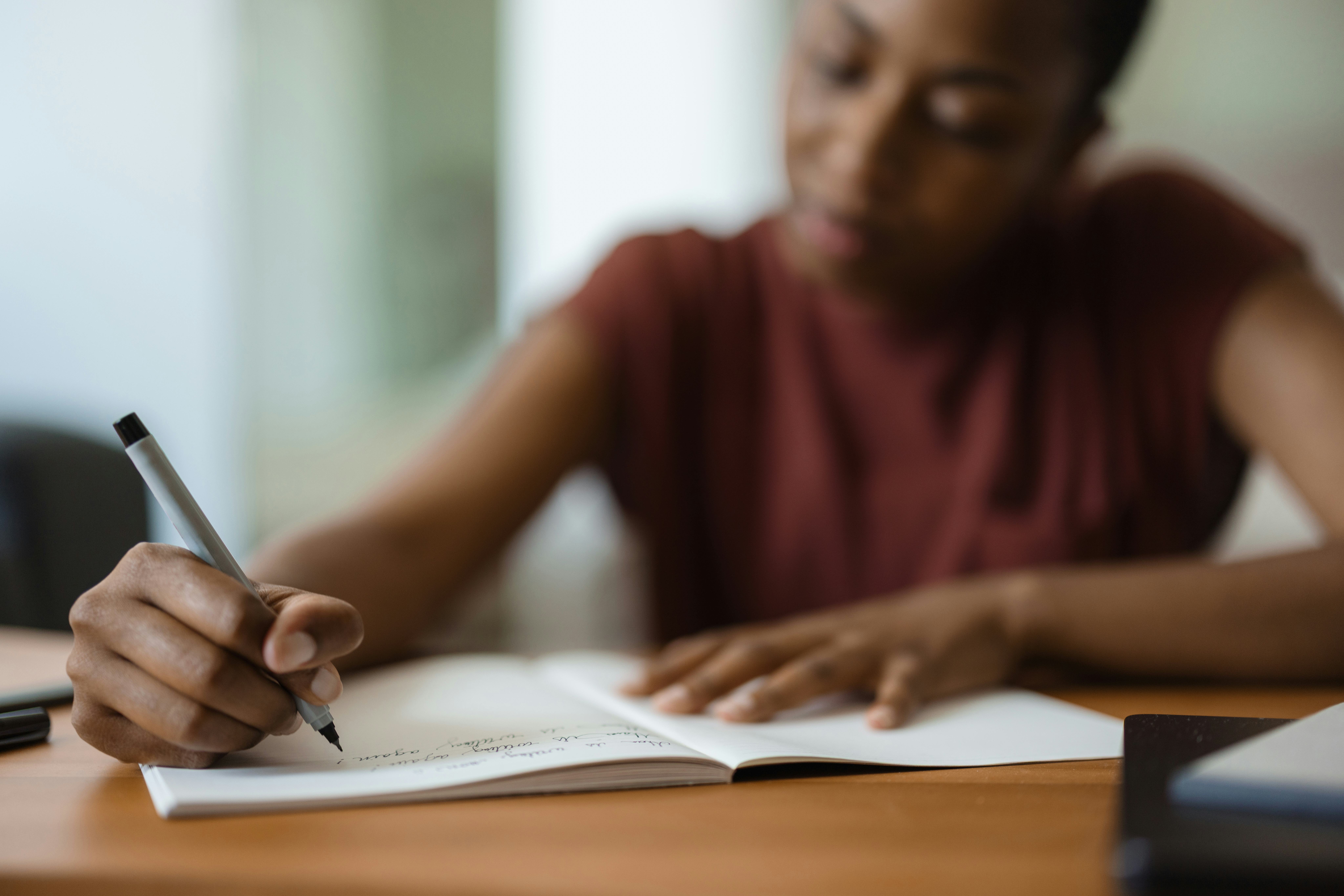 Young black woman immersed in writing notes and studying at her desk, surrounded by a cozy home envi...