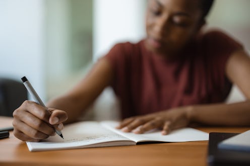 Young black woman immersed in writing notes and studying at her desk, surrounded by a cozy home envi...