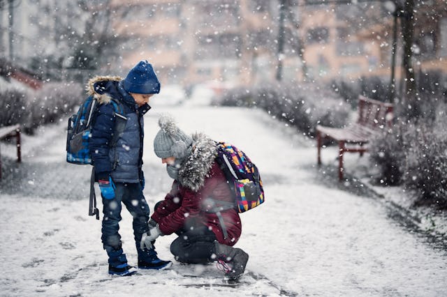 A girl stops to tie her brother's shoe as they walk to school in the snow.
