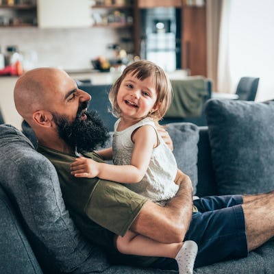 Young father and his toddler play on the couch.