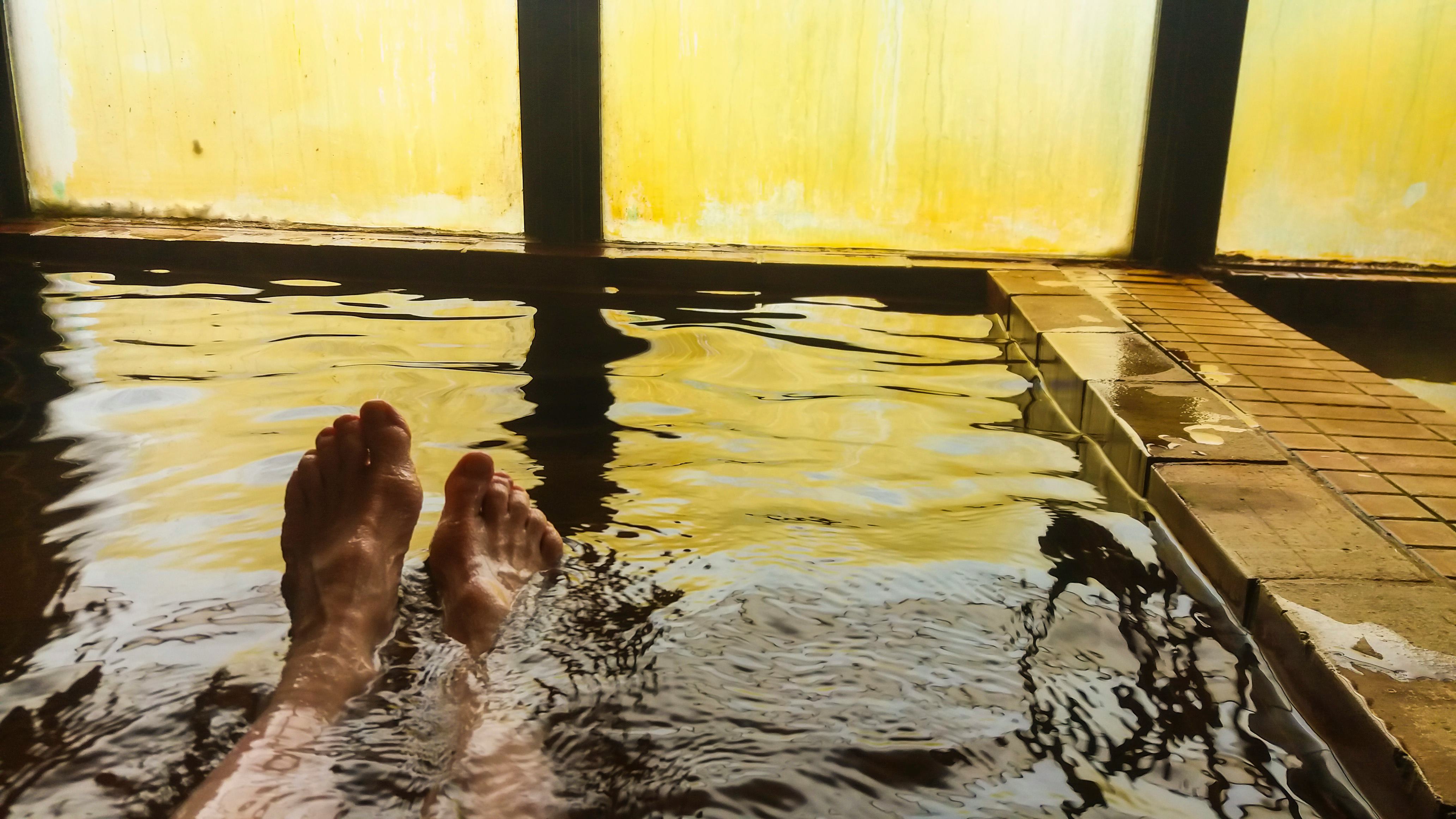 Female enjoying hot spring water against steamed window, personal perspective, just feet in water, H...