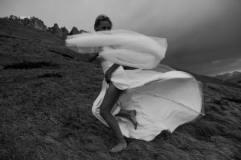 A young woman in a wedding dress joyfully runs barefoot through the grass in a mountainous landscape...