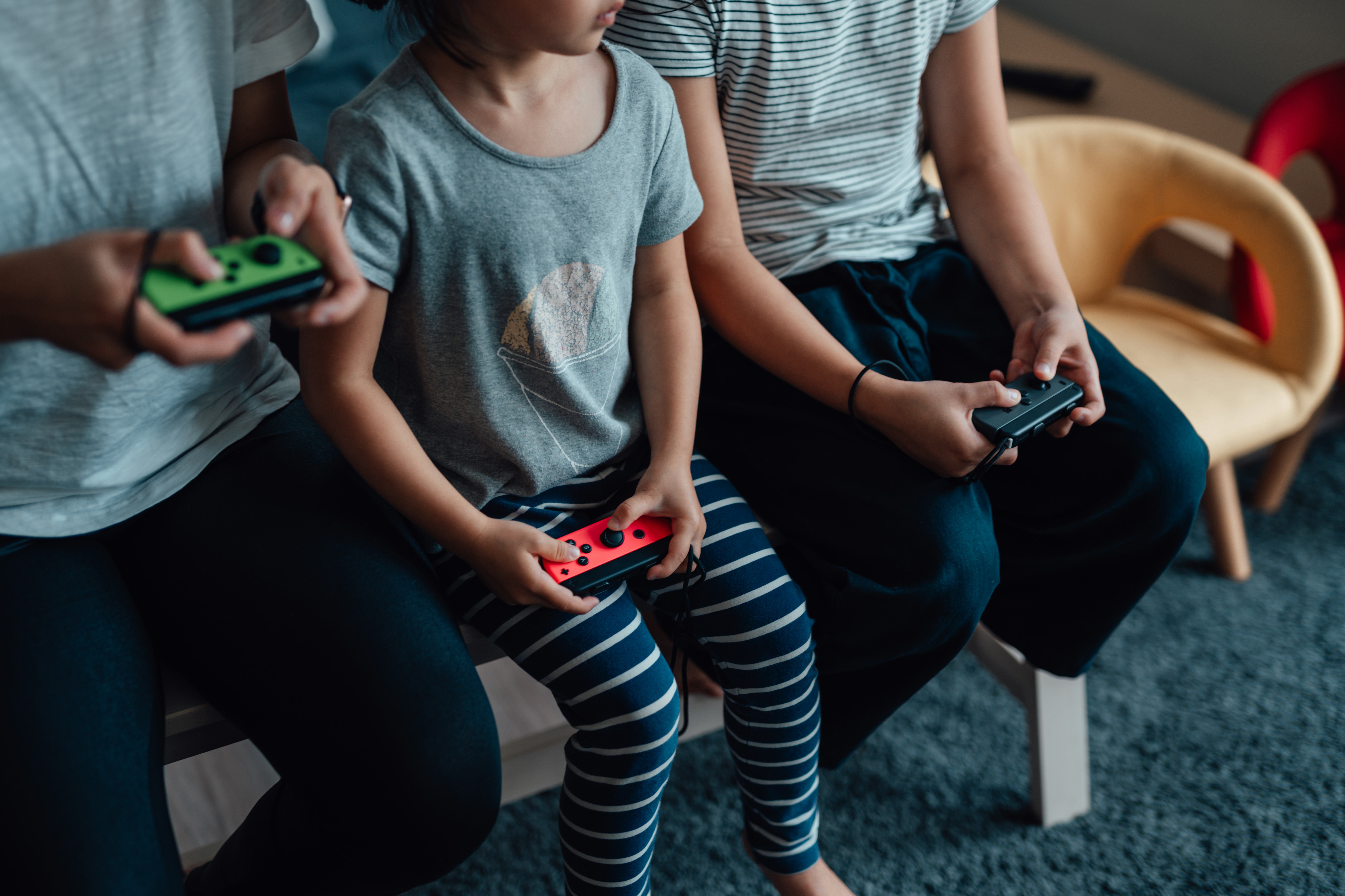 Cropped shot of mother and daughters holding game controllers, playing video games together. Enjoyin...