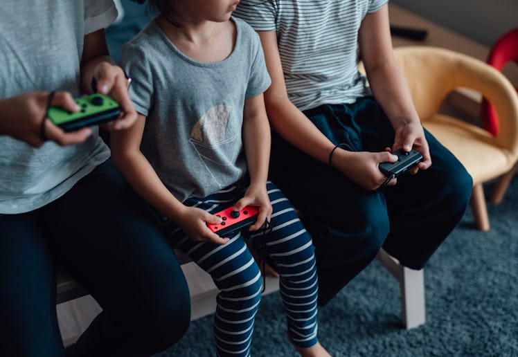 Cropped shot of mother and daughters holding game controllers, playing video games together. Enjoyin...
