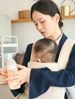 A mom prepares a bottle for her baby, which is strapped to her chest.