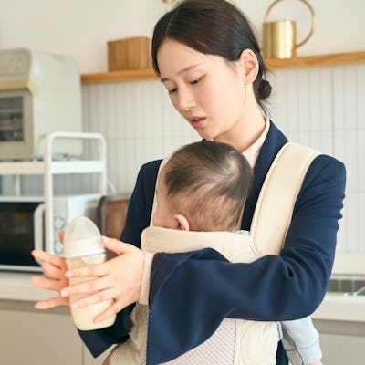A mom prepares a bottle for her baby, which is strapped to her chest.
