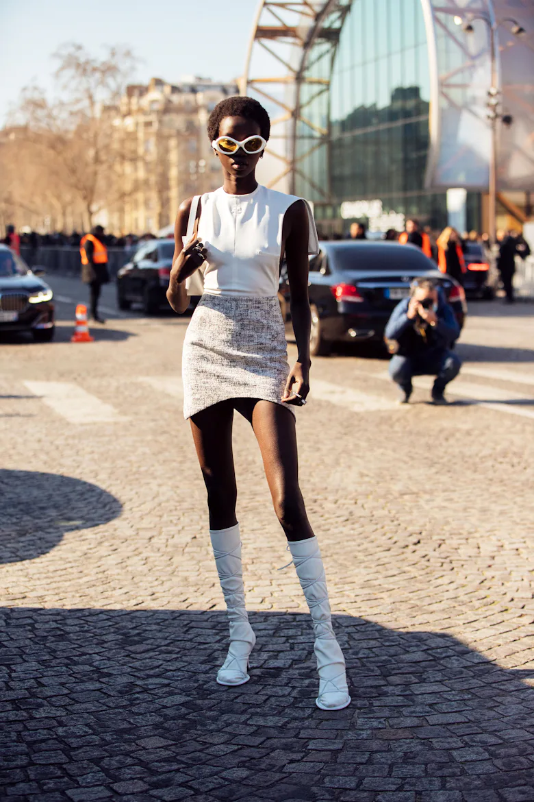 Model Anok Yai wears white alien sunglasses, a white leather assymetrical tank top, white purse, cre...