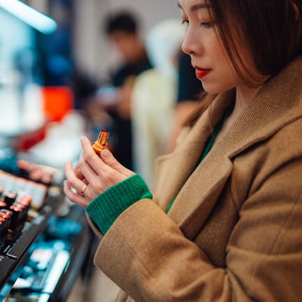 Young woman trying lipstick on hand at cosmetic store in a story about the best new beauty products ...