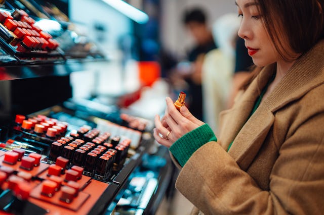 Young woman trying lipstick on hand at cosmetic store in a story about the best new beauty products ...
