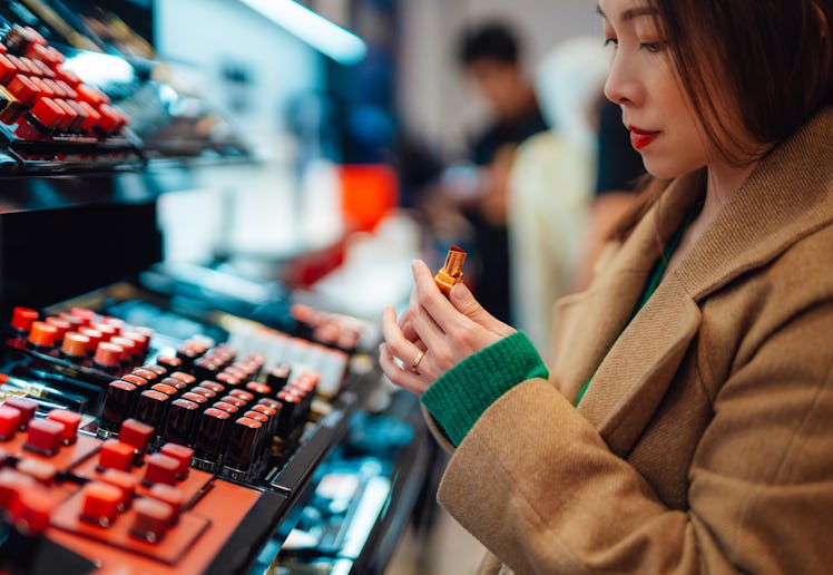 Young woman trying lipstick on hand at cosmetic store in a story about the best new beauty products ...