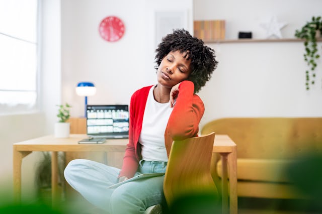 Tired freelancer dozing off at her home office desk, surrounded by a laptop and digital tablet, embo...