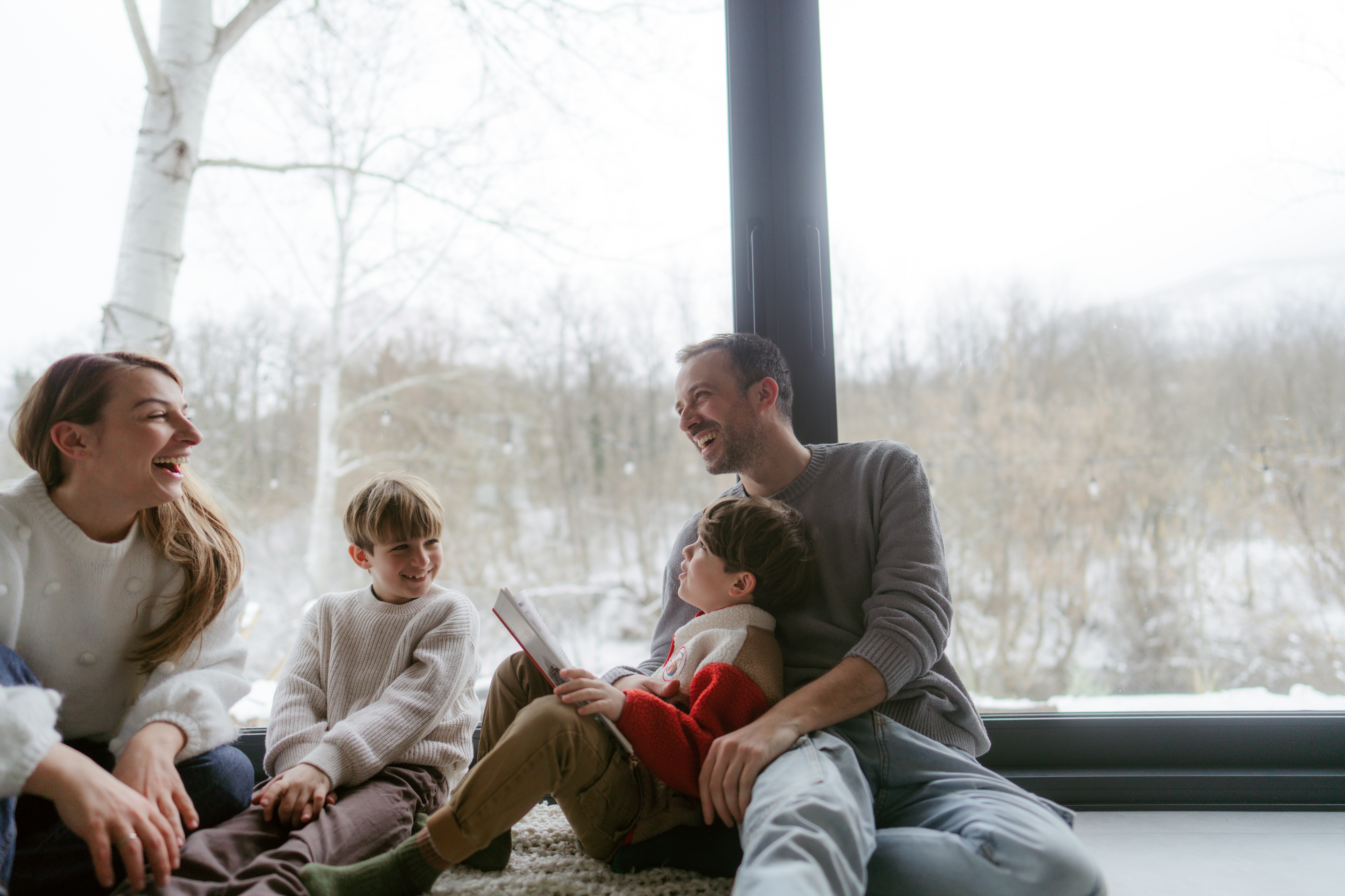 Photo of a cheerful young family, sitting in their cosy home, reading books and enjoying each others...
