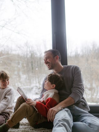 Photo of a cheerful young family, sitting in their cosy home, reading books and enjoying each others...