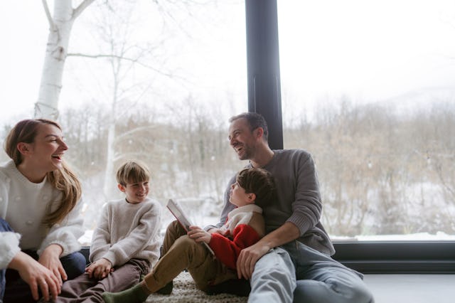 Photo of a cheerful young family, sitting in their cosy home, reading books and enjoying each others...