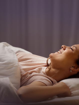 Happy woman stretching with her eyes closed in a bed.