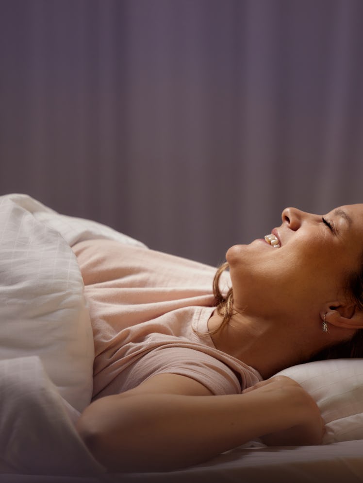 Happy woman stretching with her eyes closed in a bed.