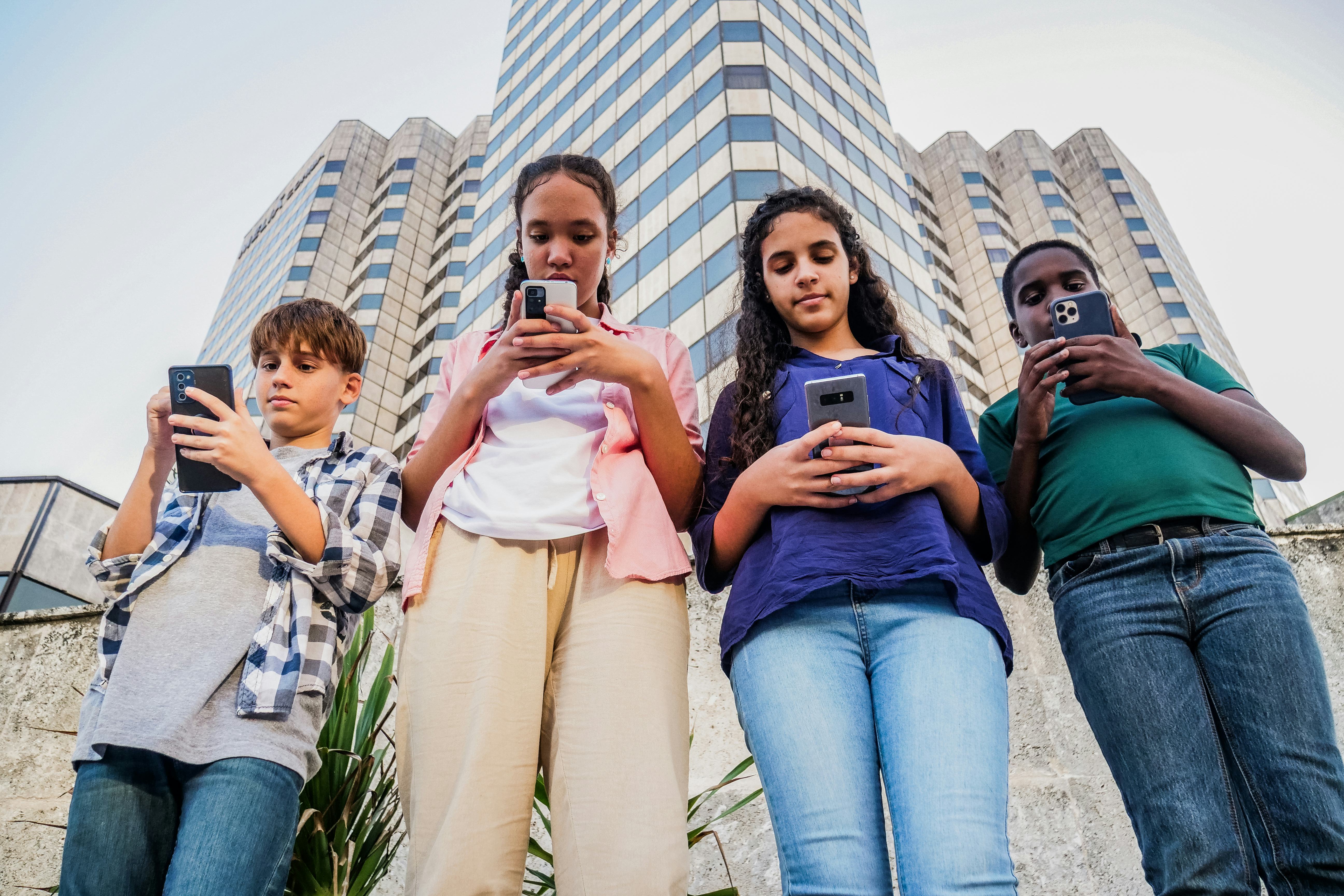 Four teenagers look down at the phones as they walk around a city. 