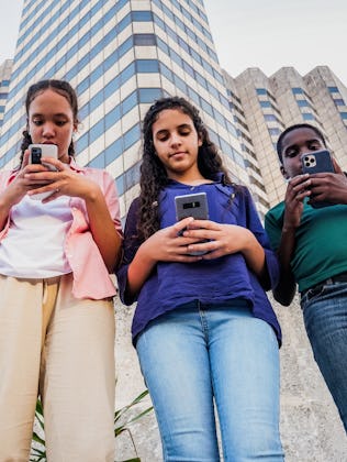 Four teenagers look down at the phones as they walk around a city.