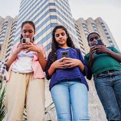 Four teenagers look down at the phones as they walk around a city.