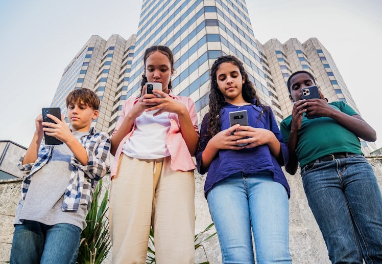 Four teenagers look down at the phones as they walk around a city.