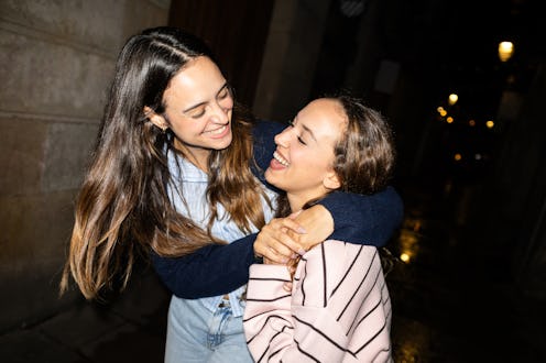 Young smiling female friends hugging laughing outdoors at night