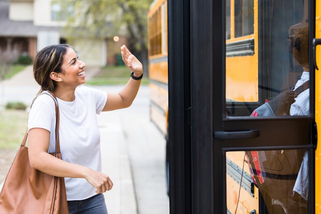 A mid adult Hispanic mom waves as her son boards a school bus on the first day of school.