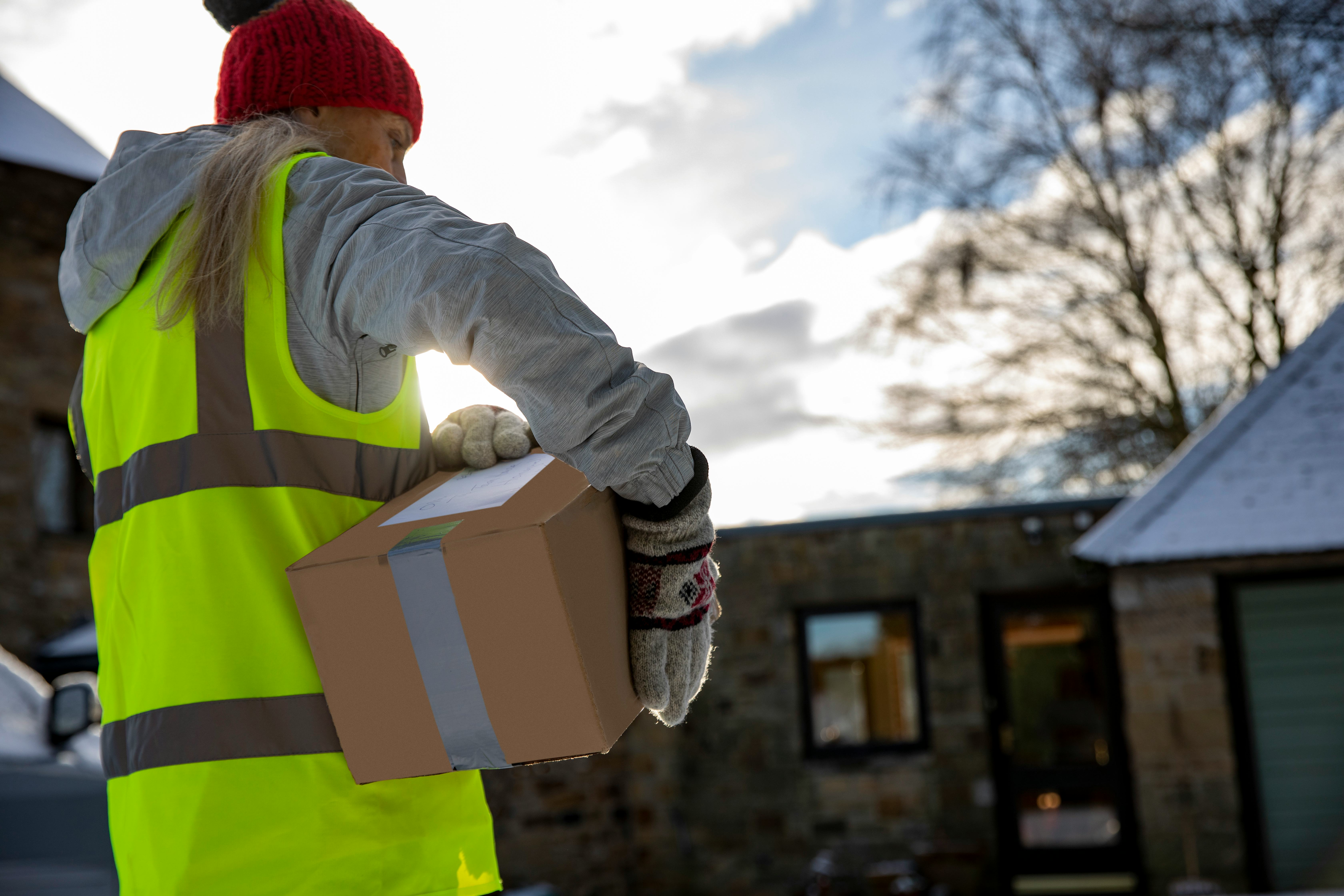 Low angle rear view of a woman holding packages under her arm while making a contactless delivery in...