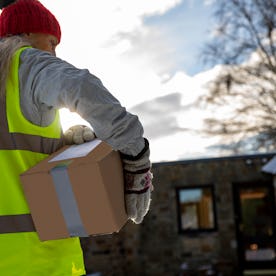 Low angle rear view of a woman holding packages under her arm while making a contactless delivery in...