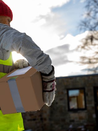 Low angle rear view of a woman holding packages under her arm while making a contactless delivery in...