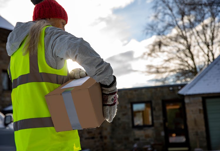 Low angle rear view of a woman holding packages under her arm while making a contactless delivery in...