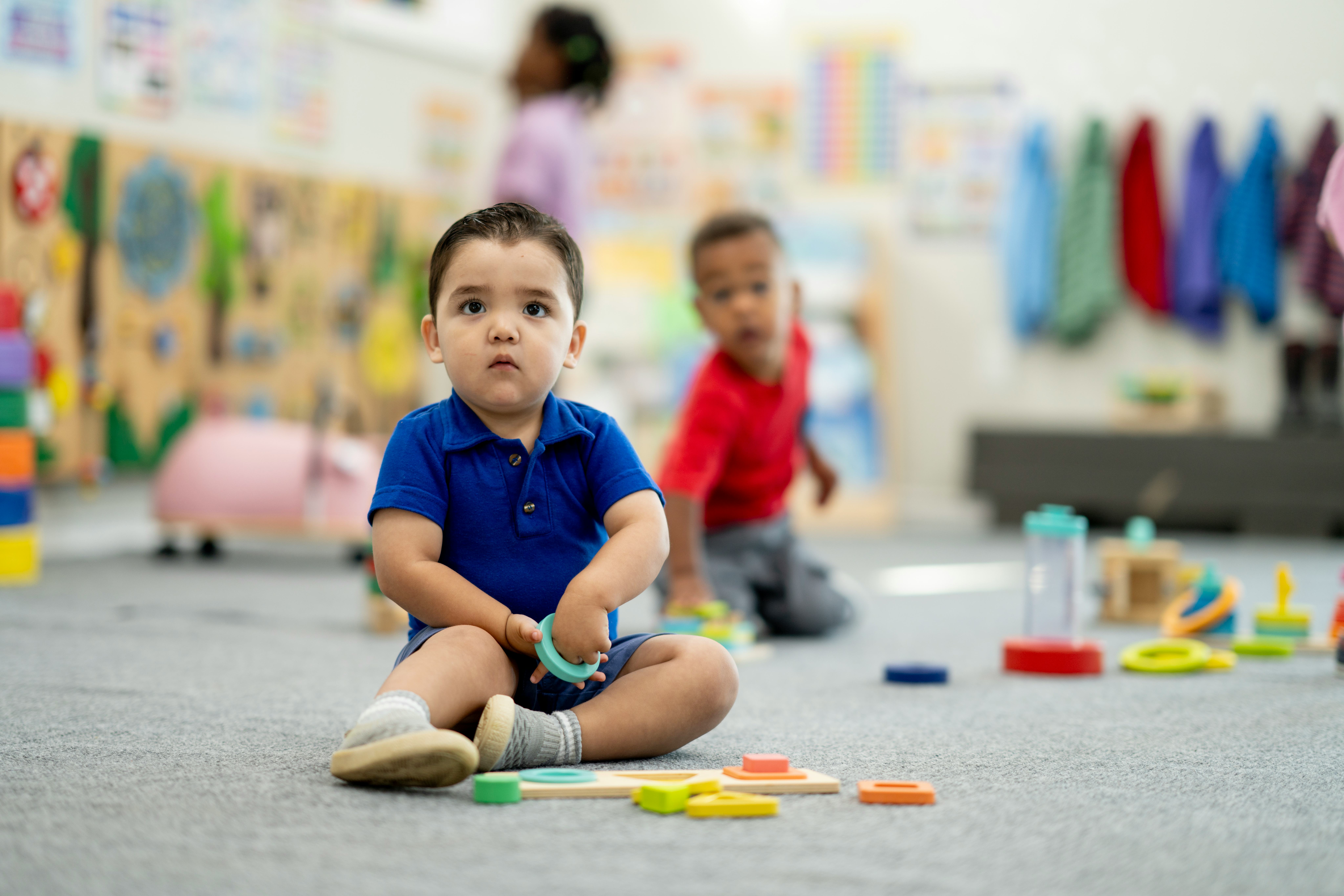 Diverse preschool scene shows curious children exploring shapes and colors with supervision, fosteri...