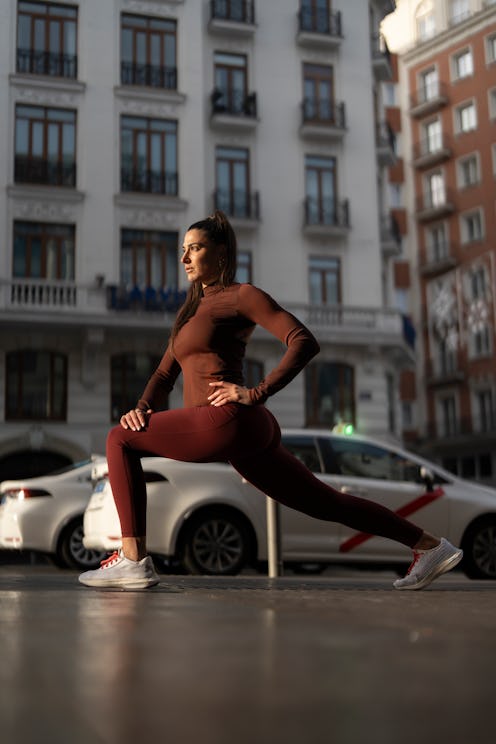 Young adult woman stretching outdoors, practicing lunge in a modern urban setting