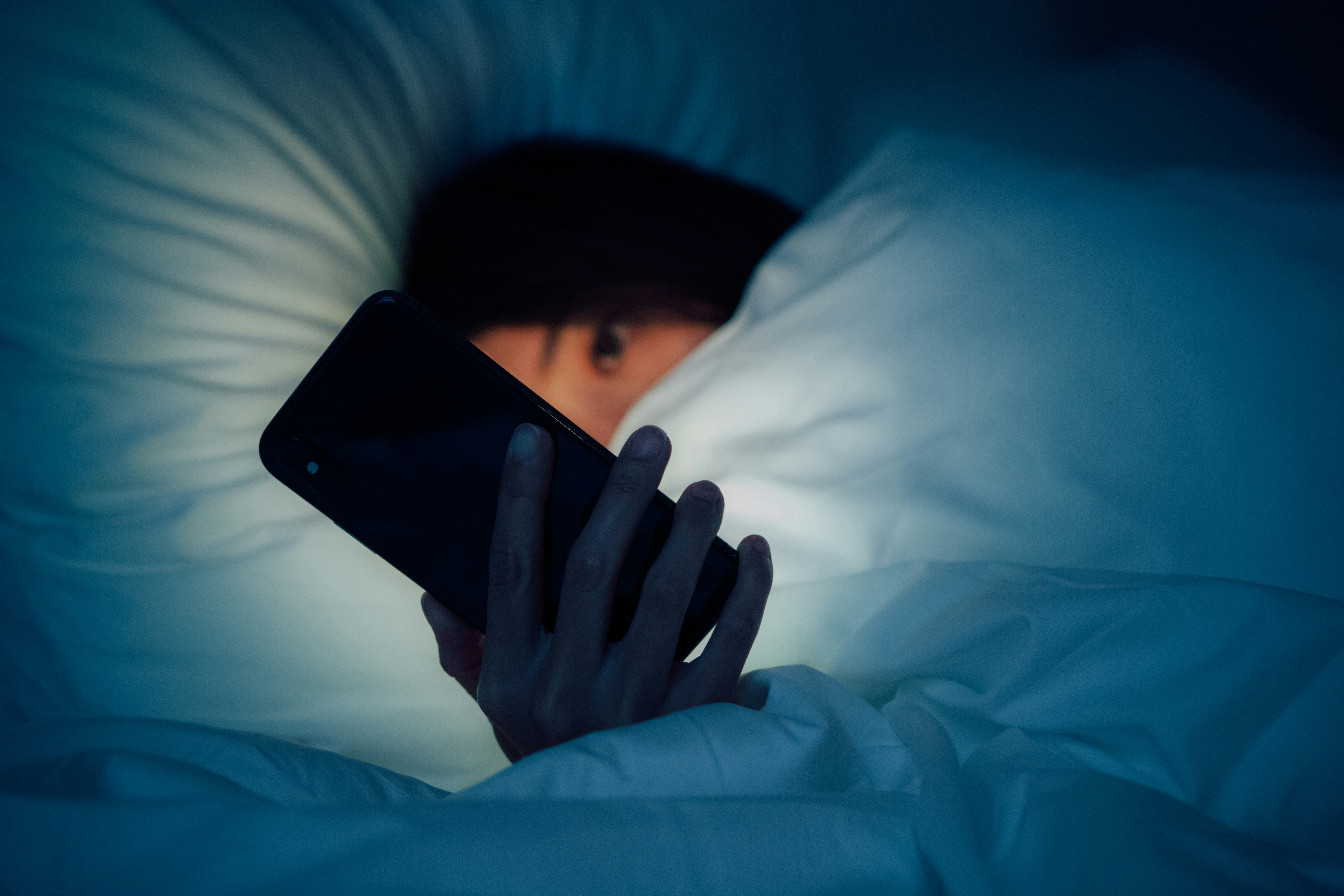 Woman hiding under the blanket, chatting and surfing the internet with smart phone at late night on ...