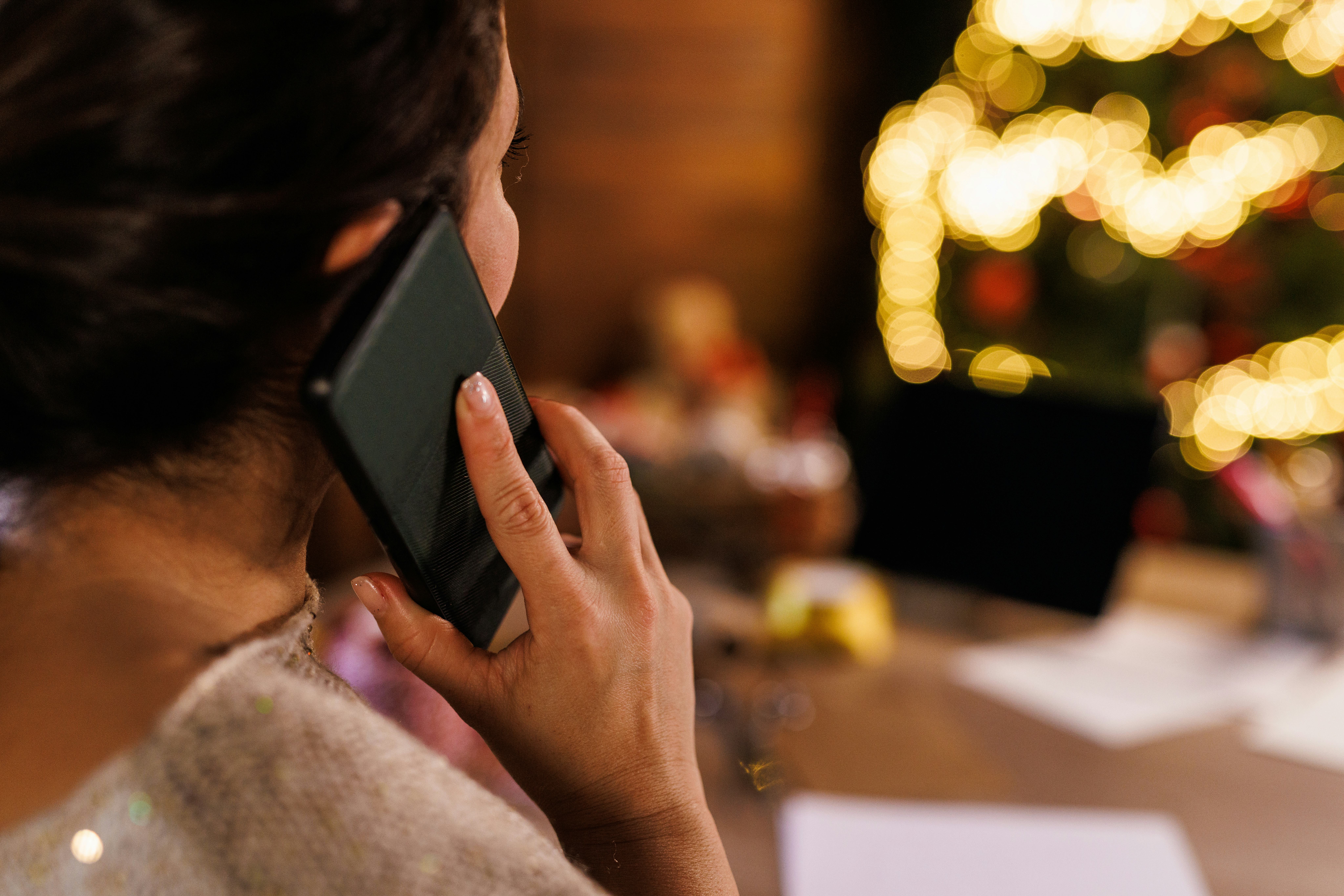 Over the shoulder view of mid adult woman sitting at the table, in front of a Christmas tree, talkin...