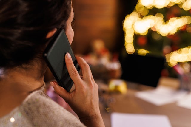 Over the shoulder view of mid adult woman sitting at the table, in front of a Christmas tree, talkin...