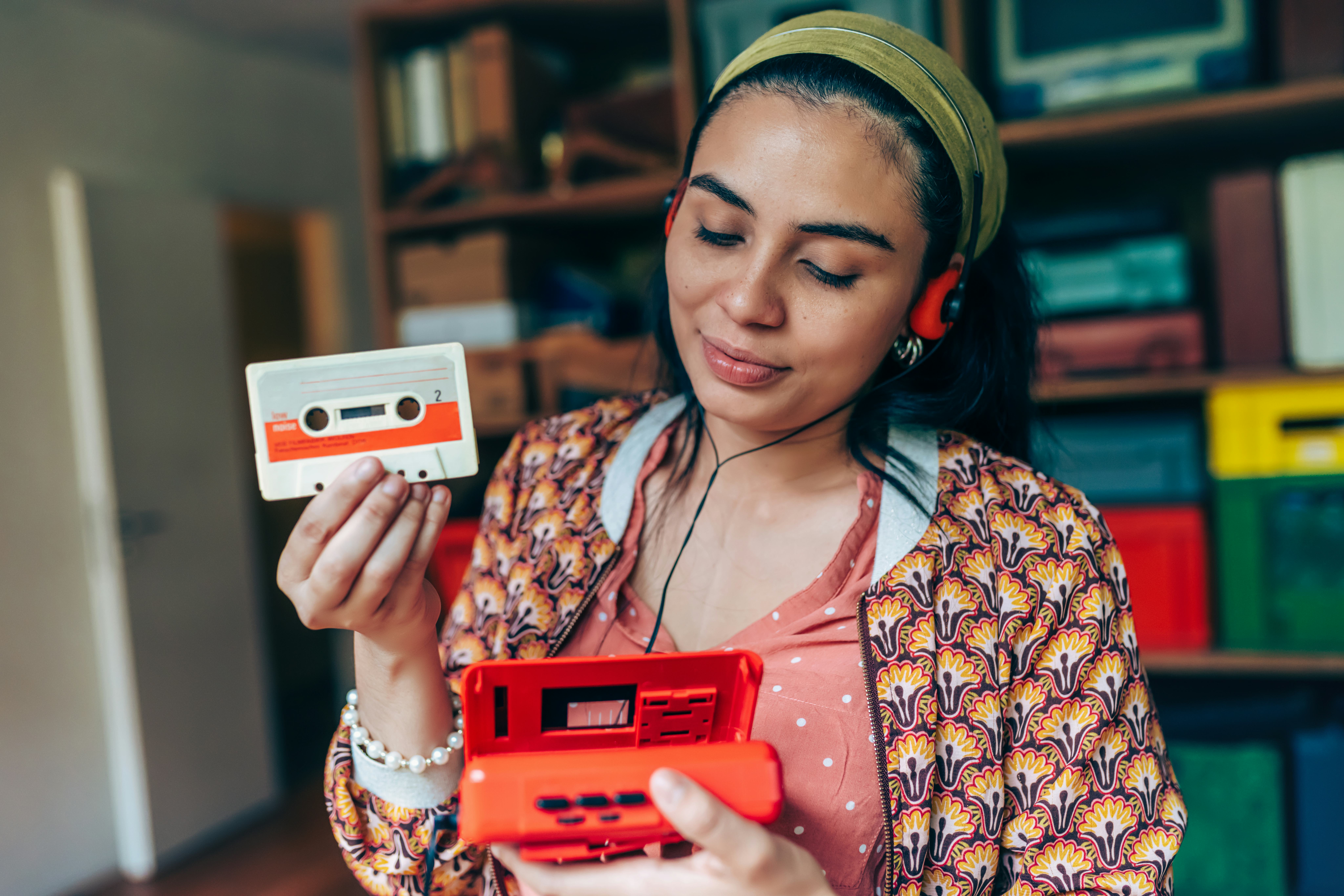portrait of young smiling woman with orange headphones putting in audio cassette  into red retro wal...