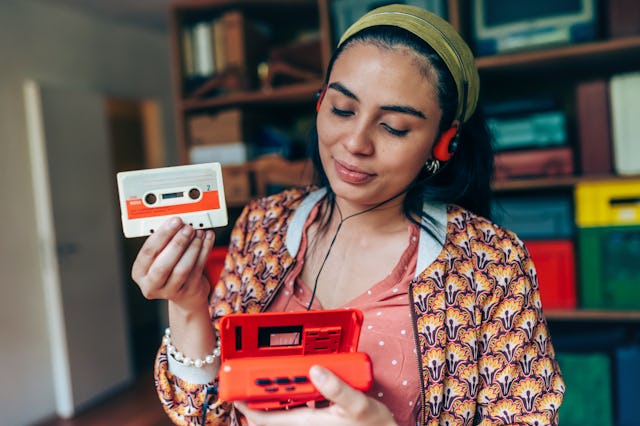 portrait of young smiling woman with orange headphones putting in audio cassette into red retro wal...