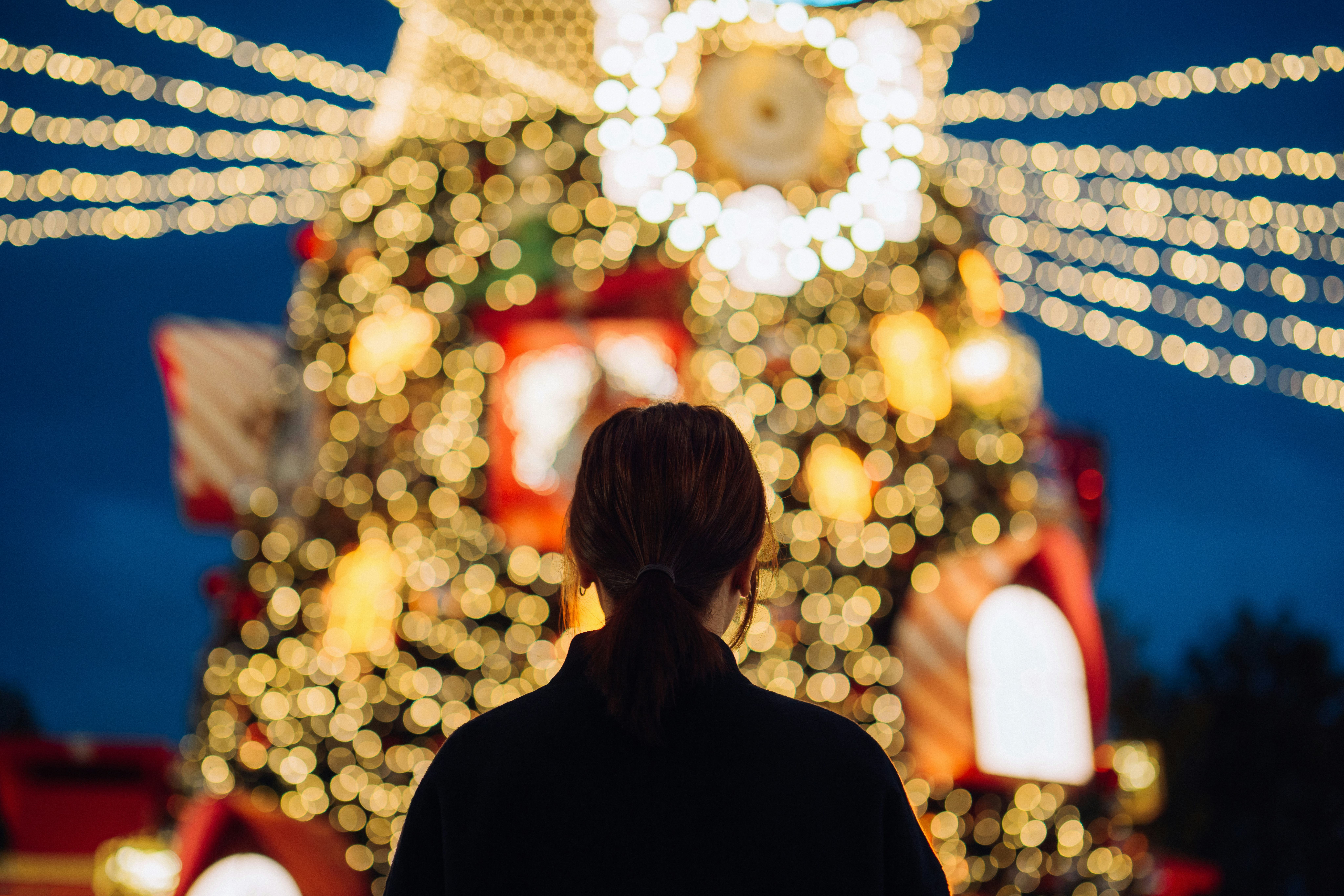 Rear view of young Asian woman looking at an illuminated Christmas tree with decorated Christmas lig...