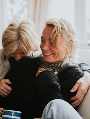 A mother hugs her adult daughter in a domestic living room. The scene is comfortable and loving as t...