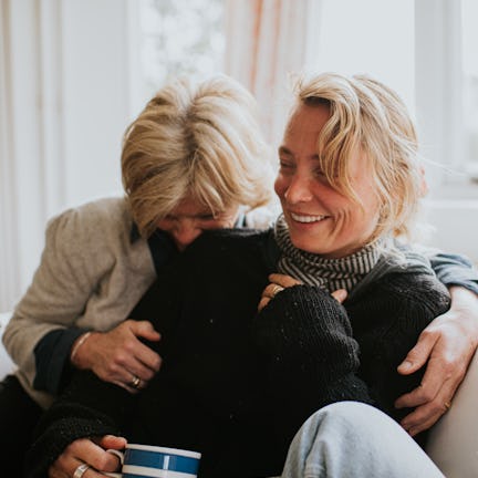 A mother hugs her adult daughter in a domestic living room. The scene is comfortable and loving as t...