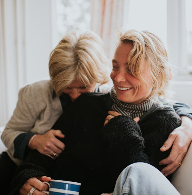 A mother hugs her adult daughter in a domestic living room. The scene is comfortable and loving as t...